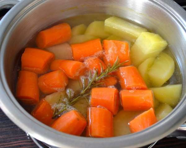 Очистить морковь и картофель. Одну морковку отложить в сторону. Остальные овощи нарезать кусочками, выложить в кастрюлю и залить холодной водой. Поставить на огонь, довести до кипения и варить 30 минут (я добавила веточку розмарина). 