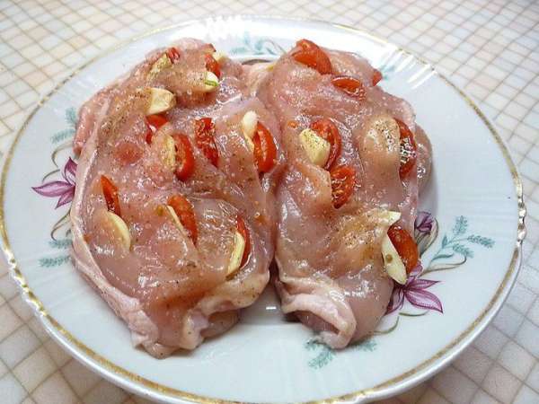 Куриные грудки промываем, просушиваем бумажным полотенцем, натираем солью и смесью специй. Помидоры моем и нарезаем небольшими пластинками. Чеснок очищаем и нарезаем дольками. На каждой грудке приподнимаем кожицу. Делаем несколько поперечных разрезов и шпигуем чесноком с помидорами. 