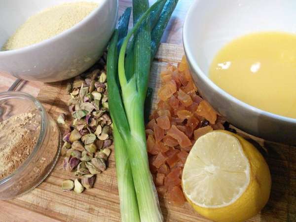 Подготовить продукты для кускуса. Курагу и инжир нарезать на кусочки, зеленый лук — колечками, фисташки крупно порубить. В пиалу влить апельсиновый сок, выдавить сок лимона. 
