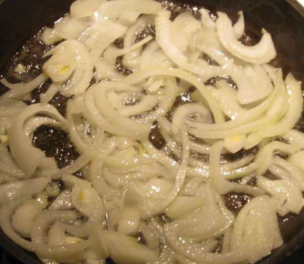В сковороду, в которой будет тушиться курица, налить оливковое масло и положить зубчик чеснока и луковицу, тонко порезанную полукольцами. Слегка обжарить до появления легкого запаха лука.