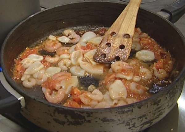 Кальмаров нарезать кольцами, а креветки и рыбу — небольшими кусочками и добавить в сковороду.
