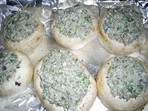 На растительном масле обжариваем мелко нарезанный лук, затем добавляем порезанные грибные ножки и извлеченную мякоть из шляпки. В последнюю очередь добавляем фарш и жарим до его готовности. Солим и приправляем по вкусу.
Еще для для начинки нам понадобится любой твердый сыр и зелень петрушки и укропа. Мне нравится, когда петрушки больше. Сыр натираем на крупной терке, половину сразу отложим, чтоб посыпать шампиньоны сверху. Добавляем мелко нарезанную зелень. Добавляем майонез и перемешиваем.
 Смешиваем все обе начинки. 
Полученной смесью начинить подготовленные шампиньоны.
