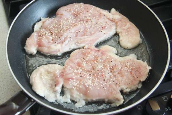 На раскаленную сковороду налить растительное масло, выложить куриные отбивные перченой стороной вниз. Теперь посолить, поперчить и посыпать кунжутом  верхнюю сторону. Жарить на сильном огне ровно 3,5 минуты.