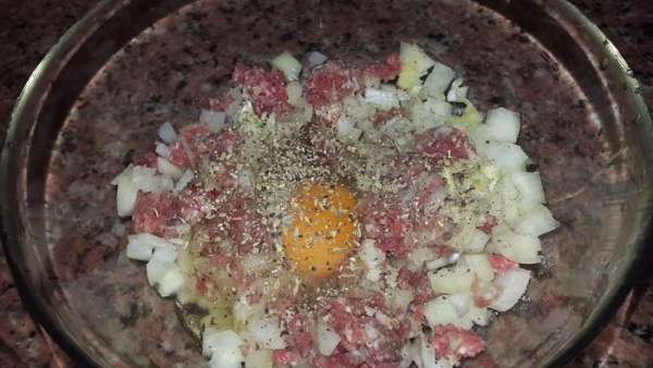 Фарш выкладываем в миску, добавляем к нему нарезанный на кубики лук, яйцо, соль, перец и травы. Тщательно перемешиваем.