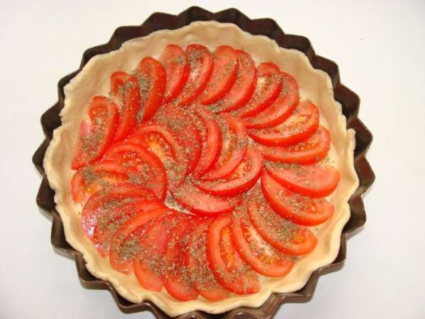 Помидоры порезать тонкими дольками, выложить одним слоем поверх теста, присыпать сухим майораном и слегка солью.