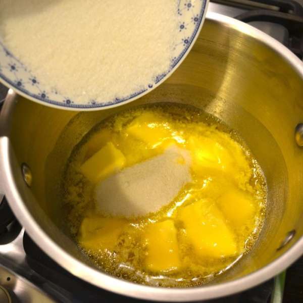 Первым делом шоколад нарезать небольшими кусочками. В ковшике поставить закипать молоко. А в небольшую кастрюльку положить сливочное масло, порезанное кусочками и поставить на огонь. Как только масло начнет таять, добавить сахар и перемешать. 