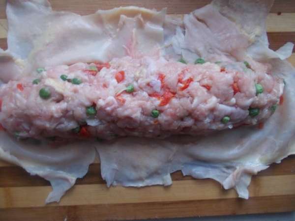 Разравниваем кожу курицы на столе и формируем колбаску,плотно ее укладывая.