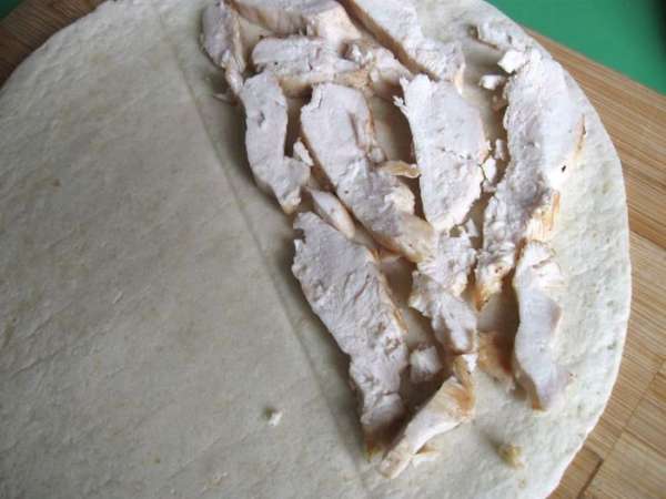 Дать курице немного остыть, нарезать пластинами, распределить кусочки курицы между двумя тортильями, положив на половинки лепешек.