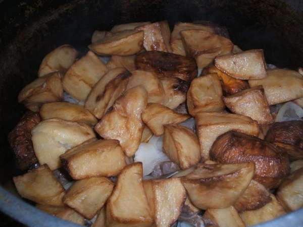 Затем нарезаем полукольцами лук, кладем поверх мяса и сверху выкладываем наш жаренный картофель. Накрываем крышкой, убавляем газ до минимума и томим так около 1 час.