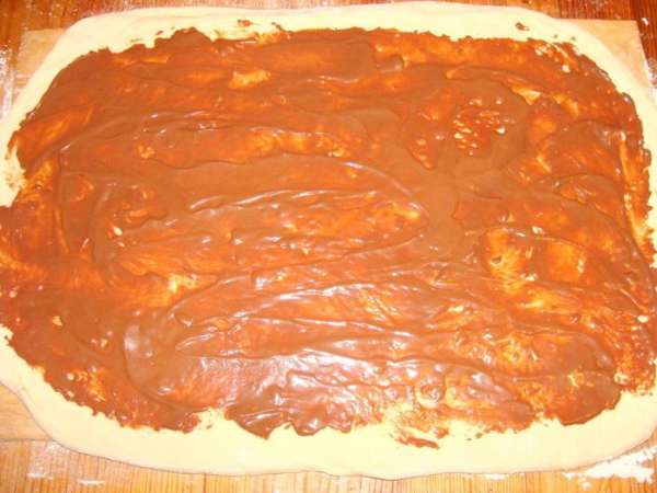 Шоколадные конфеты типа 'Маски' и шоколад растопить на водяной бане, смешать со сметаной и сахарной пудрой. Остудить. 1/2 частью смазать тесто, оставляя края по 1.5-2 см.
