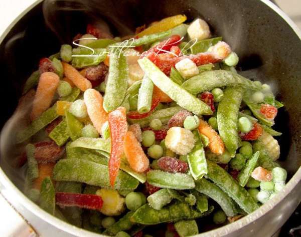 К мясу добавить смесь замороженных овощей, посыпать красным перцем. Тушить до полуготовности. 
