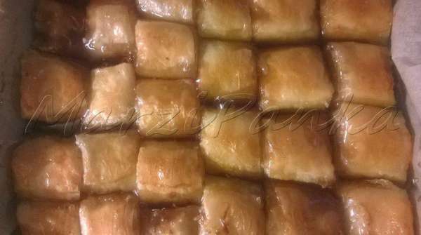 Готовую баклаву вынуть из духовки. Аккуратно придерживая подручными средствами содержимое формы, чтобы не соскользнуло, сливаем все масло в чашку (его можно будет использовать еще раз).

И сразу же поливаем холодным сиропом 