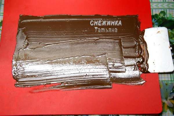Для начала займёмся ШОКОЛАДНЫМИ УКРАШЕНИЯМИ. Их даже можно приготовить заранее, они хорошо хранятся в холодильнике, в контейнере с плотно закрывающейся крышкой. Итак, топим шоколад на водяной бане. Наносим тонкий слой шоколада при помощи шпателя на рабочую поверхность, у меня это гибкая доска, лучше же использовать мраморную или нейлоновую поверхность. Отправляем в холодильник, чтобы слой подзастыл. Нужно дождаться момента, когда шоколад перестанет быть мягким, но не затвердеет окончательно. Я поняла, что если, дотрагиваясь до шоколада, след пальца не остаётся, то он готов.