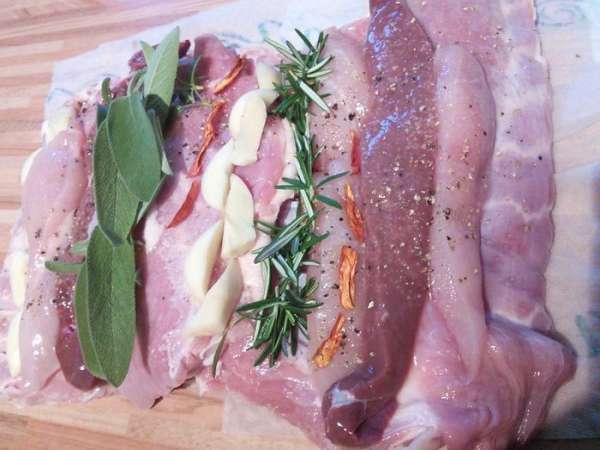 Мясо я купила уже запакованное в чулок. Когда делаю простую буженину, проделываю ножом дырки и шпигую мясо с разных сторон. Тут задача усложнилась и мне пришлось чулок для начала снять. Мясо распластала по столу, это брюшко поросёнка. Разложила куриную грудку, порезав ее вдоль на 2 части, так же печенку, сняла иголочки с розмарина, выложила в ряд, так же поступила с шалфеем (его можно заменить на лавровый лист), чеснок порезала на части, из него сделала 2 рядка, т. ж. перчик чили. Хорошенько посолила и поперчила. 