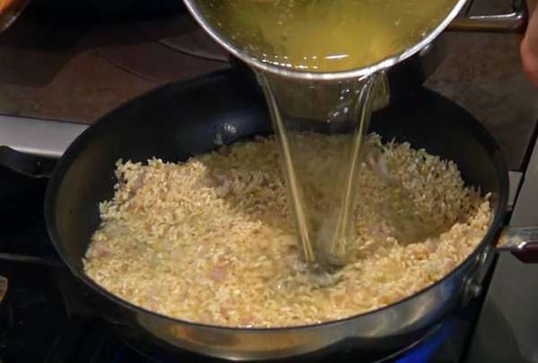 Рис всыпать в сковороду с луком и чесноком, перемешать и дать ему пропитаться маслом, влить пару половников куриного бульона, все перемешать, затем влить еще куриного бульона, так чтобы рис был полностью покрыт, и прогревать на небольшом огне до готовности.